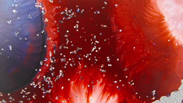 Red and navy blue ink mixing in water with sparkling glitter, creating a cosmic nebula effect