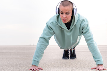  Concentrated young woman with sports headphones doing push-ups.