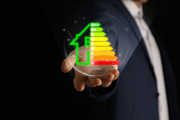 Energy efficiency. Man holding virtual colorful rating against black background, closeup