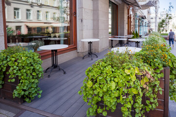 Fototapeta na wymiar The summer outdoor urban cafe with white tables and plants installed between the tables.