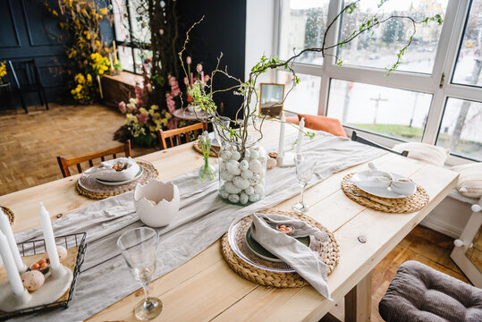 Setting table for Easter dinner with candle, ceramic plates with easter eggs in nest, bunny made of linen napkin. Holidays celebration concept. Decor with vase with twig, branch, leave at home. Set up