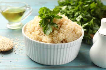 Tasty quinoa porridge with parsley in bowl on light blue wooden table, closeup