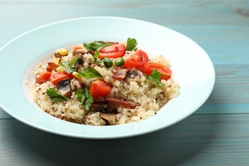Plate of tasty quinoa porridge with fried bacon, mushrooms and vegetables on light blue wooden table, closeup