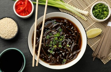 Fototapeta na wymiar Tasty soup with buckwheat noodles (soba), ingredients and chopsticks on dark grey table, flat lay