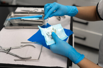 Close-up of the dentist's hand opens a sterile package with clamps. Dental instruments are on the...