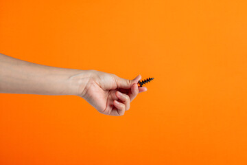 A black screw in hand on orange background.