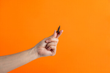 A black screw in hand on orange background. - obrazy, fototapety, plakaty