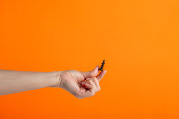 A black screw in hand on orange background. - obrazy, fototapety, plakaty