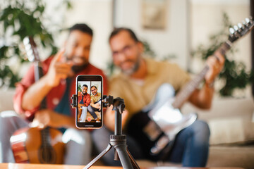 Best friends, musician jamming together, making video on social media. Playing music on guitar together at home for fans. Concept of male friendship, bromance.