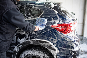 Professional car wash. Worker washes the vehicle body with foam. Stock photo
