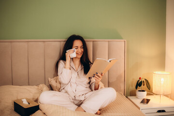 Sad woman crying while she reading a good paper book sitting on a sofa at home. Upset girl read...