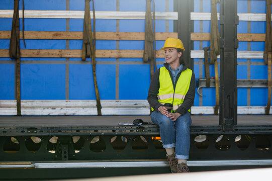 Female warehouse receiver in reflective vest and helmet sitting inside of truck in cargo area, trailer.