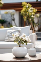 Outdoor living area design with beautiful flowers in the white vase and soft white sofa. 