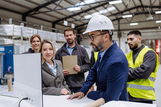 Manager presenting project to full team of warehouse employees on computer. Team of workers, managers, female director in modern industrial factory, heavy industry, manufactrury.