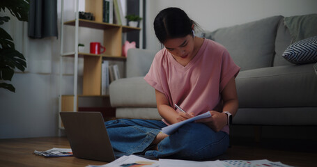 Portrait of Young woman sitting on the floor working with a laptop and checking workpaper at home office.