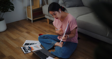 Portrait of Young woman sitting on the floor holding documents video call presentation on laptop at home office.