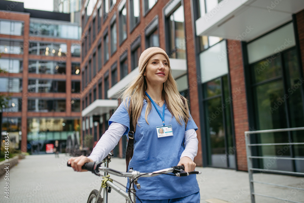 Wall mural beautiful nurse commuting through the city by bike. doctor city commuter traveling from work by bike