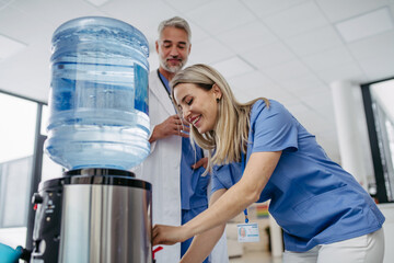 Doctor and nurse taking a break during work shift at hospital, drinking water from water dispenser...
