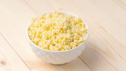 Millet porridge in white cup on wooden background, selective focus