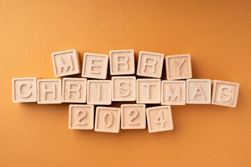 A flat New Year composition made of wooden cubes with the text Merry Christmas 2024. Christmas concept. Greeting card for winter holidays. Layout, flat lay