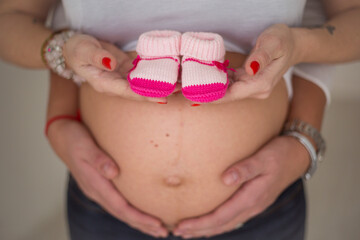 woman with shoes on belly, hands hold booties and pregnant belly