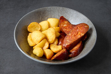 fried sausage with baked potatoes in a bowl on dark background