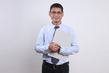 Portrait of successful Asian businessman in formal shirt and glasses looking at camera confidently while holding clipboard