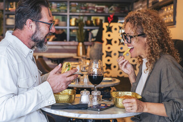 Happy couple smiling and talking in a burger pub restaurant - Married couple having lunch break at cafe bar - Lifestyle concept with man and a woman going out on weekend day