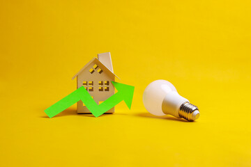 Green growing up arrow symbol, white LED light bulb and a house miniature on yellow background....