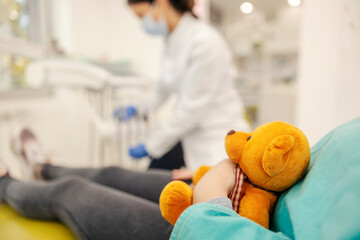 Close up of a girl's hands holding a teddy bear at dentist office.