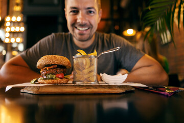 Selective focus on a delicious burger and food with a happy man in a blurry background.