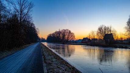 This tranquil image captures the crisp beauty of a winter morning beside a canal. The path running...