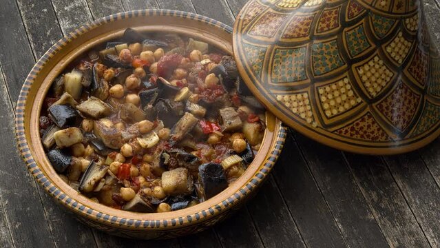 Traditional Moroccan tagine pot standing on a rustic wooden table that has just been opened. Boiling vegan tagine made of eggplant and chickpea inside. 