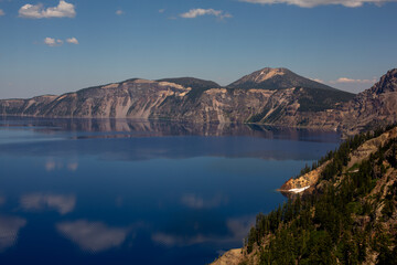 Tranquil Crater Lake, nestled among towering pines, reflects a picturesque snow-capped volcano.