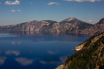 Obraz premium Tranquil Crater Lake, nestled among towering pines, reflects a picturesque snow-capped volcano.