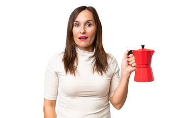 Middle-aged caucasian woman holding coffee pot over isolated background with surprise and shocked facial expression