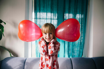 Playful girl holding balloons over ears at home