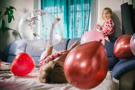 Happy sisters playing with balloons on sofa at home