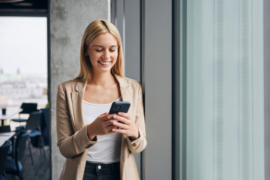 Happy businesswoman using smart phone near window in office