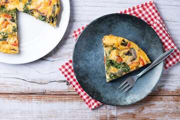 Italian Frittata made with spinach, tomatoes, onion and peppers on white wooden table