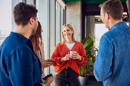 Happy businesswoman holding coffee cup and discussing with colleagues in office