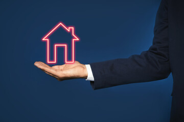 Fototapeta na wymiar Mortgage rate. Man holding illustration of house on dark blue background, closeup