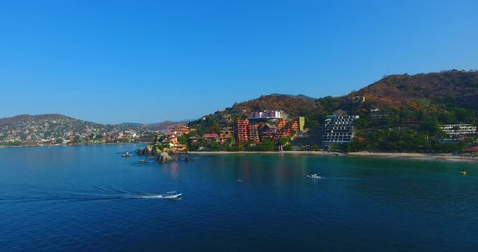 Aerial video flying by the gorgeous shoreline filled with boats, white sand beaches, and the beautiful city of Zihuatanejo, Mexico
