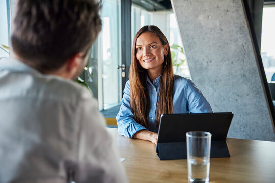 Happy recruiter sitting with tablet PC and taking job interview of candidate in office