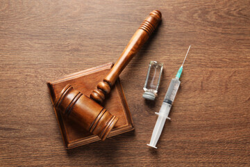 Law concept. Gavel, syringe and glass vial on wooden table, top view
