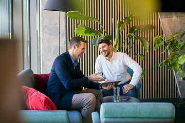 Smiling businessmen discussing over tablet PC in office lobby