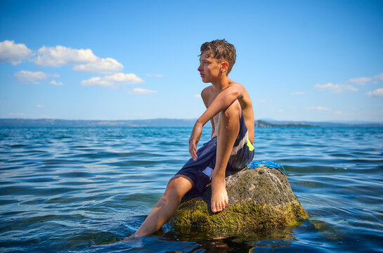 Boy sitting on rock in lake Bolsena, Italy