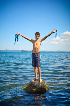 Smiling boy with arms outstretched standing on rock in lake Bolsena, Italy