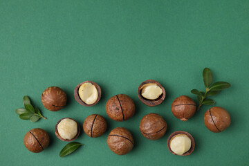 Tasty Macadamia nuts and leaves on green background, flat lay. Space for text