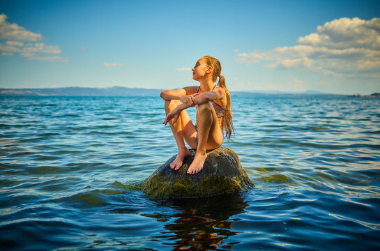 Girl sitting on rock in Lake Bolsena, Italy